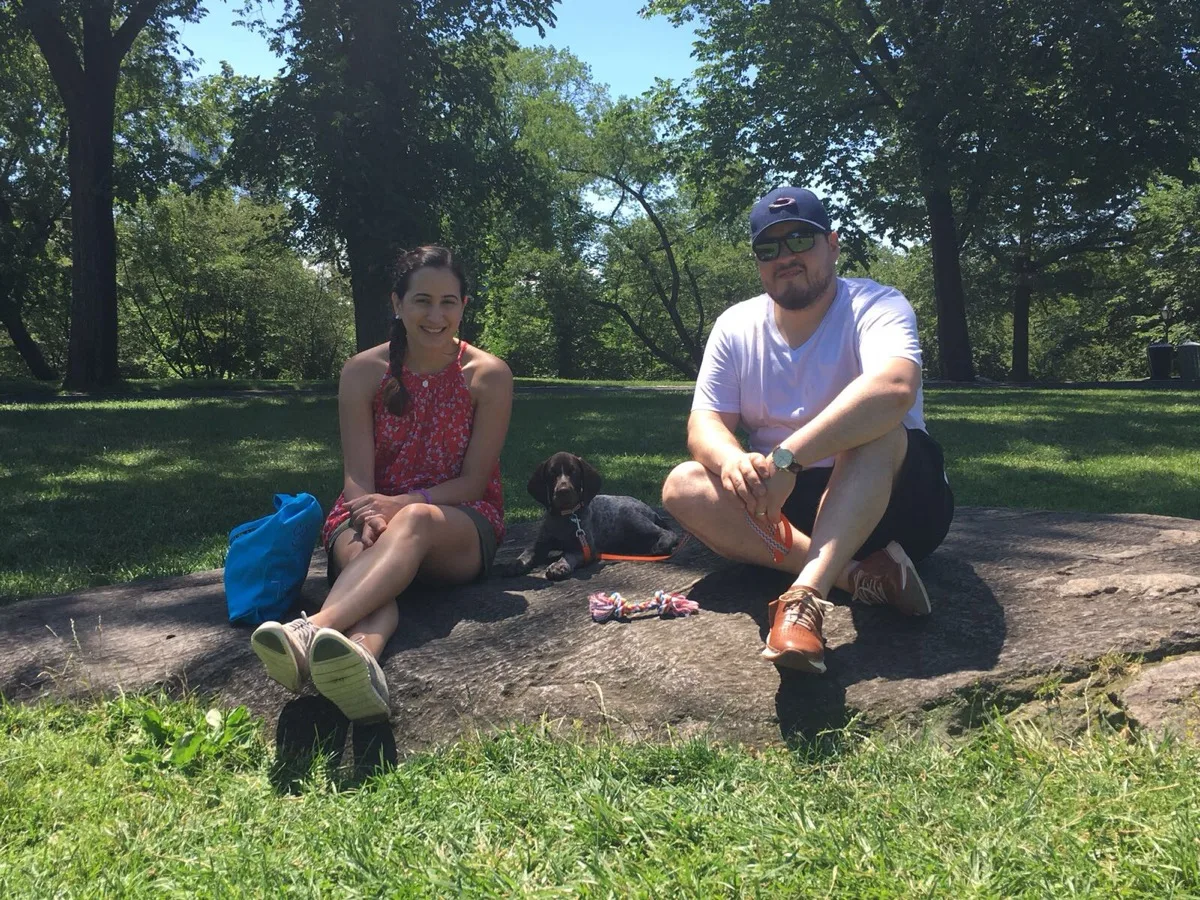 Gus and Marian sitting on a rock in Central Park with puppy Ollie between them, June 2017