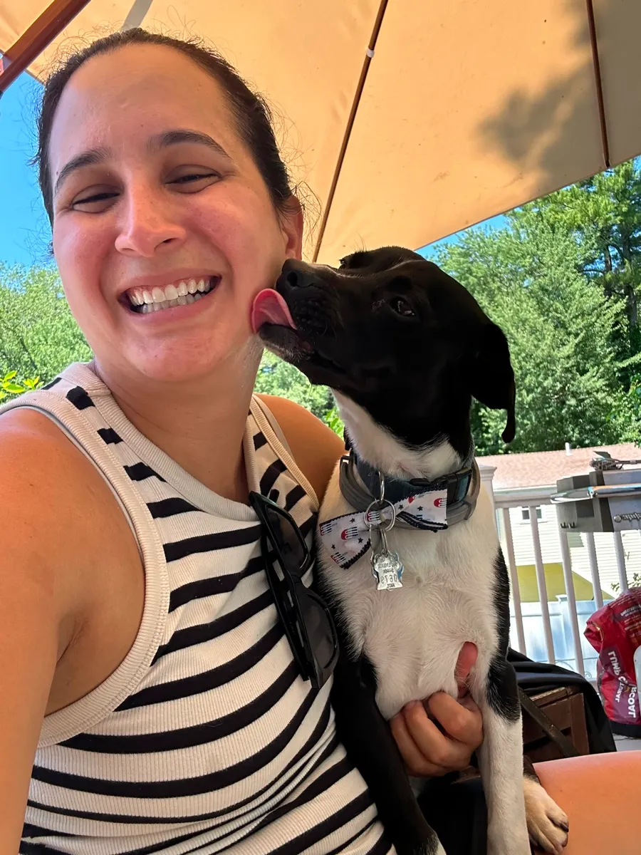Marian laughing as a black and white puppy licks her cheek under the patio umbrella